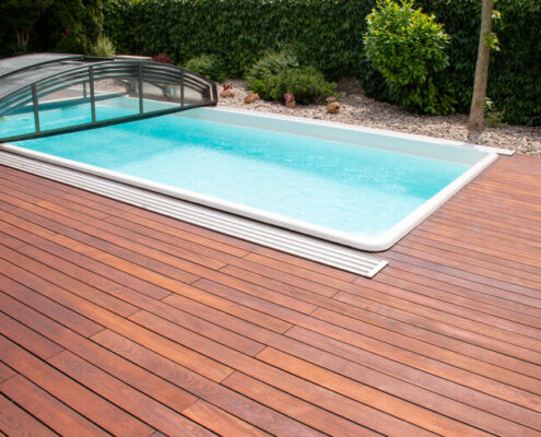 Außenschwimmbad mit Überdachung und Teakholz-Deck, exotische Teakholz-Bodenbeläge in Streifen um den Pool