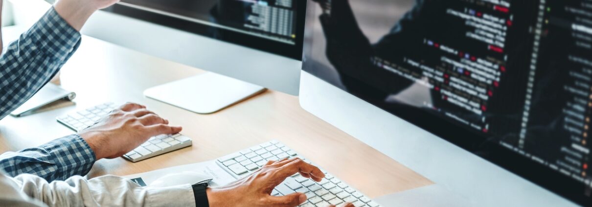 Zwei Entwickler programmieren gemeinsam an mehreren Monitoren mit sichtbarem Code