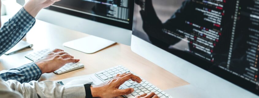 Zwei Entwickler programmieren gemeinsam an mehreren Monitoren mit sichtbarem Code