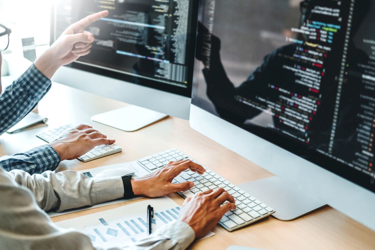 IT-Team programmiert und testet eine Produktionsplanung Software mit mehreren Monitoren und Quellcode im Fokus