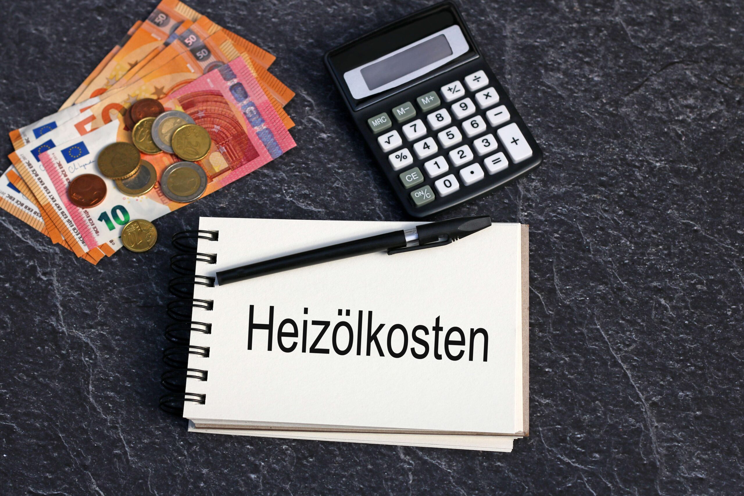 Das Wort Heizölkosten auf einen Notizblock geschrieben mit Euro Geldscheinen und Taschenrechner. 