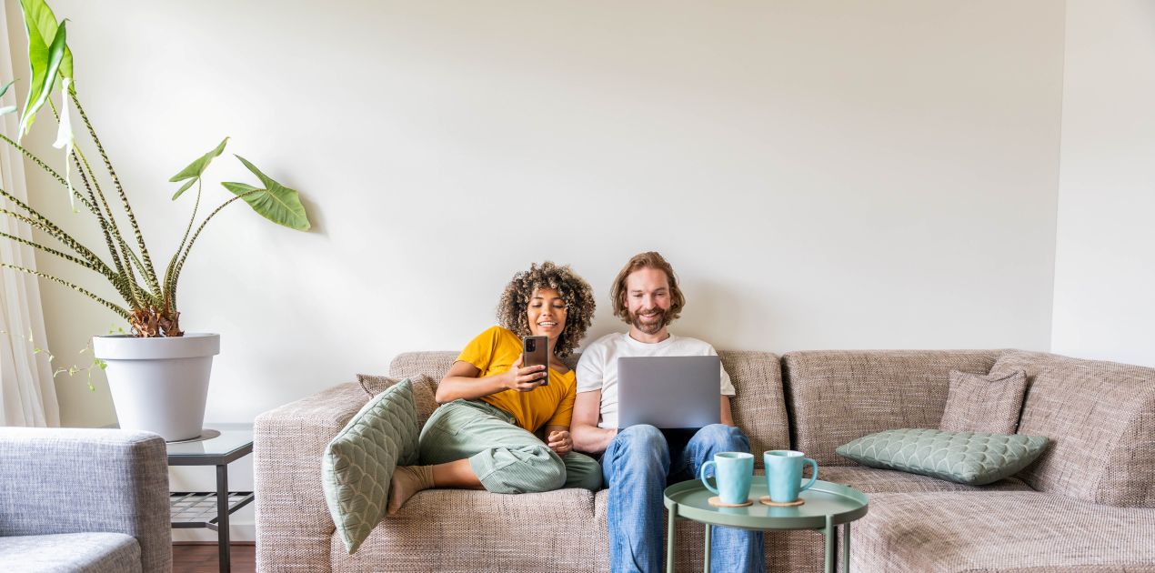 Paar auf dem Sofa nutzt stabiles Internet mit Smartphone und Laptop – moeglich durch hochwertiges FTTH Zubehoer