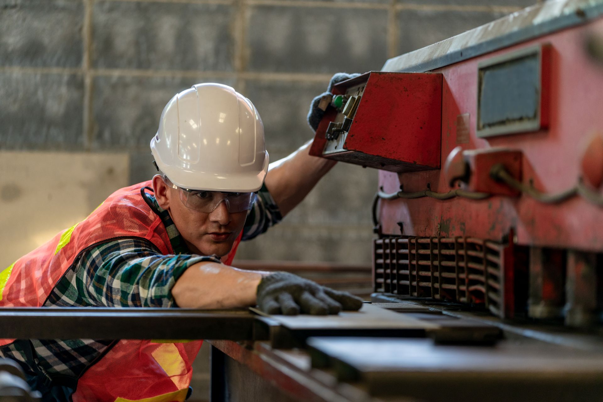 Techniker mit Helm prüft eine gebrauchte Industriemaschine auf Funktion – zeigt sorgfältige Bewertung vor dem Kauf einer gebrauchten Schneidemaschine