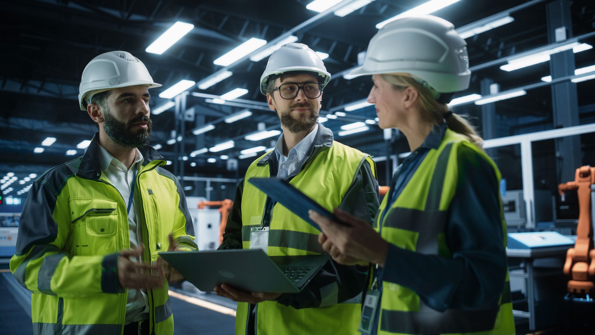 Drei Fachkräfte in Schutzkleidung bei einer Besprechung in einer modernen Produktionshalle – symbolisiert professionelle Vorbereitung beim Maschinenkauf